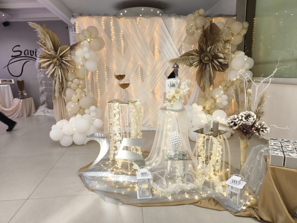 Elegante allestimento per 25° anniversario con decorazioni bianche e oro, palloncini, luci e torta celebrativa nella sala eventi Savini a Ragusa