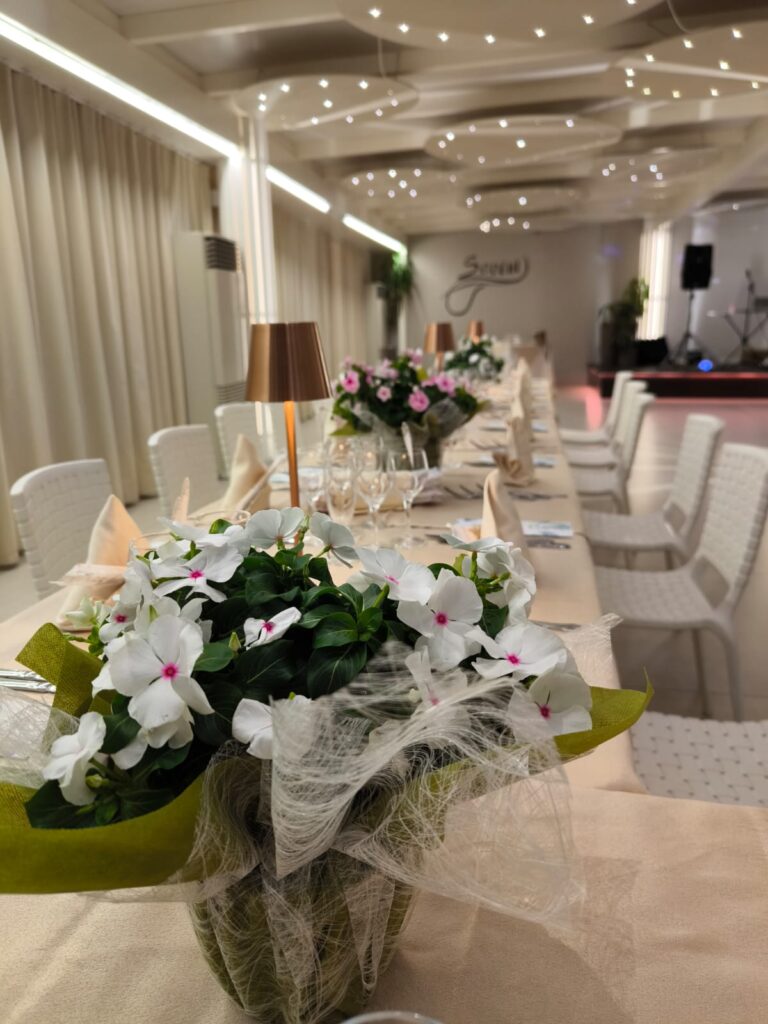 Tavolo lungo elegantemente allestito con fiori freschi e luci soffuse nella sala eventi di Savini Bar a Ragusa, ideale per cerimonie e cene speciali