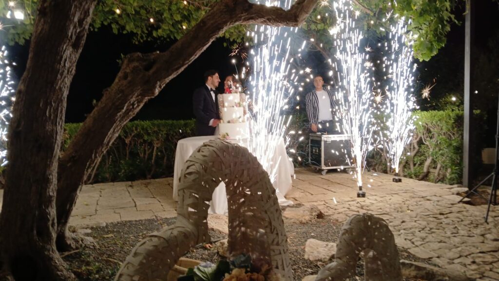 Sposi durante il taglio della torta nuziale con spettacolo pirotecnico serale nel giardino esterno di Savini Bar a Ragusa